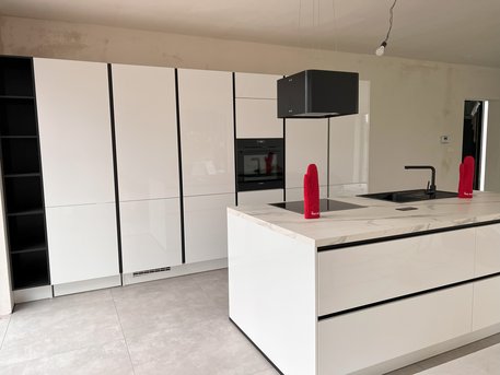 Referenzküche in Alpinweiß Hochglanz mit Griffmulden in Schwarz und versteckter Durchgangstür von Ihrem Küchenstudio in Aachen